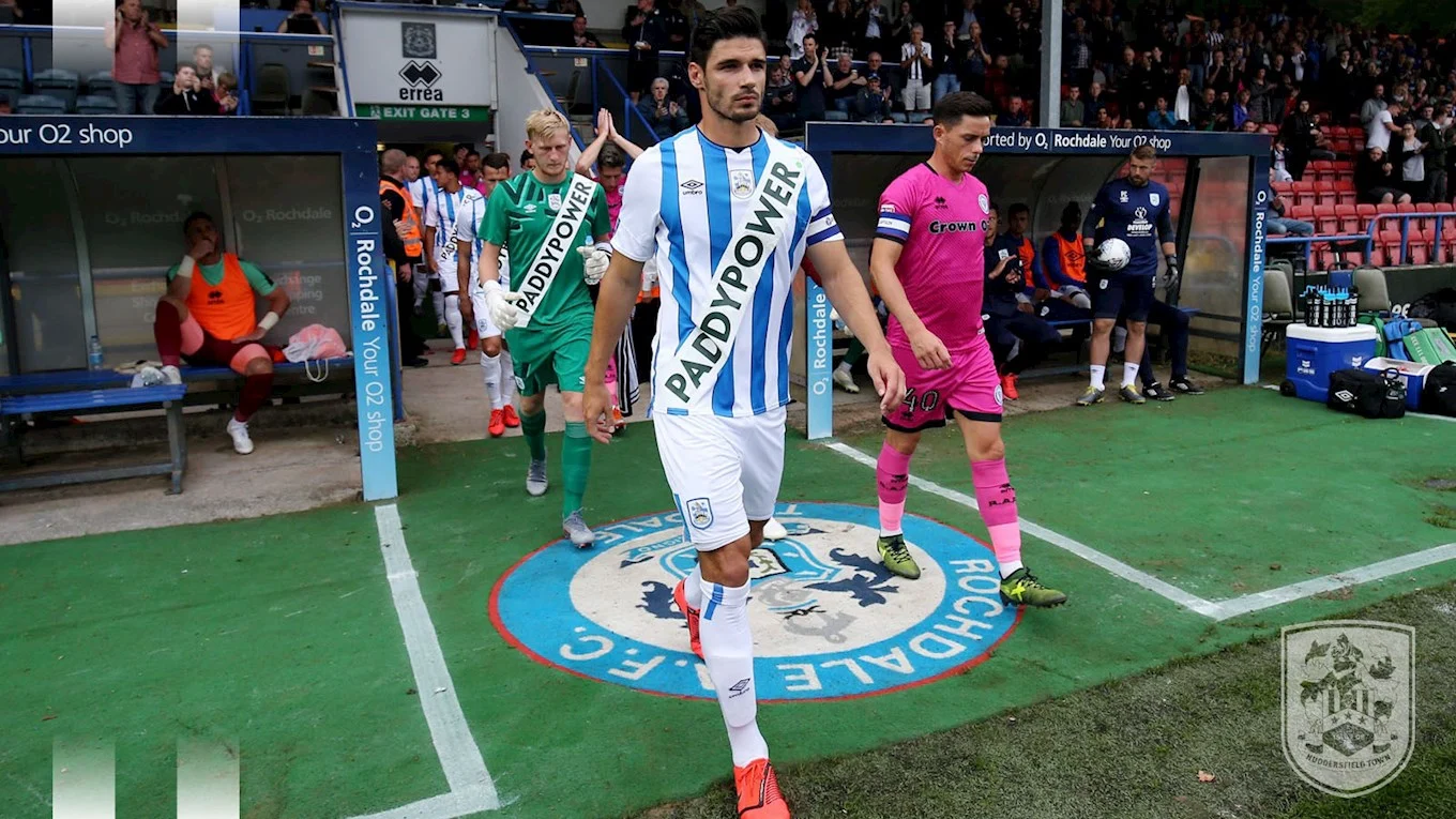 Huddersfield Town players walking out at Rochdale wearing the over-branded kit, watched by a confused crowd.